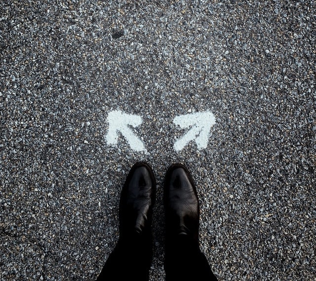 Feet standing before two arrows in different directions (Photo by Jon Tyson on Unsplash)